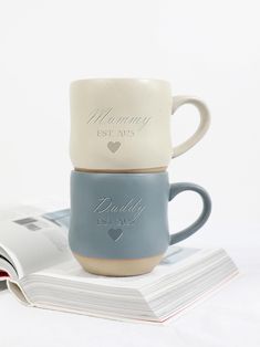 two coffee mugs sitting on top of each other next to an open book and magazine