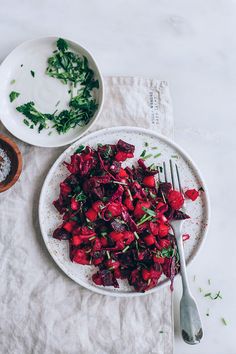 a white plate topped with beets and greens next to a bowl of seasoning