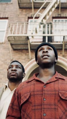 two men standing next to each other in front of a building with a fire escape