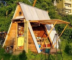 a small house made out of wood with a metal roof in the middle of some grass