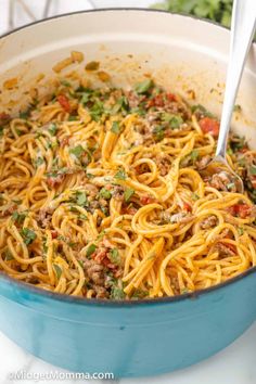 a blue pot filled with spaghetti and meat on top of a white counter next to a silver spoon