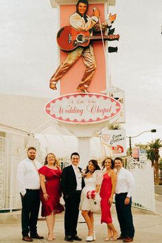 a group of people standing in front of a sign for a wedding chapel with a guitar player on it