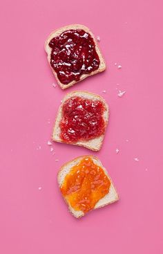 two pieces of bread with jam on them and one slice cut in half sitting on a pink surface