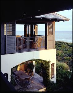 an outdoor dining area with table and chairs overlooking the ocean in front of a house