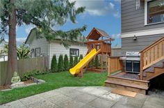 a backyard with a yellow slide in the grass next to a wooden deck and fence