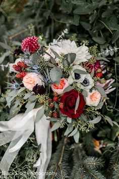 a bridal bouquet with red and white flowers, greenery and berries on it