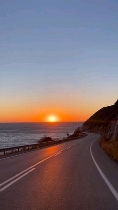 the sun is setting over the ocean and road