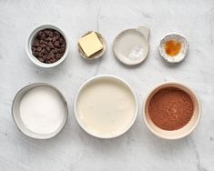 the ingredients for chocolate cake laid out in bowls on a white counter top, including milk, sugar, and cocoa