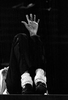 black and white photograph of person sitting on bench with hand raised up to the sky