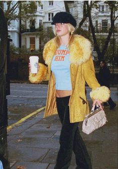 a woman walking down the street with a cup in her hand and a fur coat over her shoulders