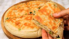 a person holding a piece of food in front of a pizza on a wooden plate