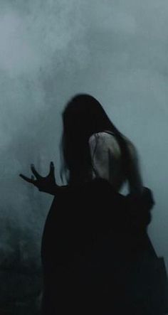 a woman standing in the fog with her hands out and looking at something behind her