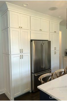 a kitchen with white cabinets and stainless steel refrigerator freezer combo in the center, surrounded by chairs