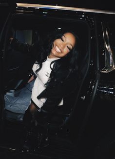 a woman sitting in the passenger seat of a black car with her arm out and smiling