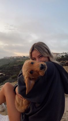 a woman sitting on the beach holding a dog wrapped in a blanket over her head