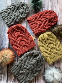 four knitted hats with pom - poms laid out on a wooden surface