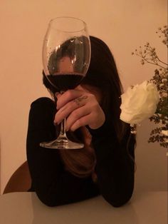 a woman sitting at a table with a glass of wine in front of her face