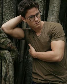 a man with glasses leaning against a tree