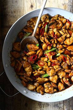 a white bowl filled with chicken and vegetables on top of a wooden table next to a spoon