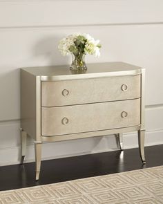 a white dresser with two drawers and a vase on top of it next to a wall