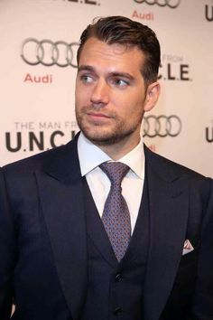 a man wearing a suit and tie standing in front of an audi logo wallpaper