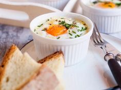 two bowls of food on a plate with bread and utensils next to it