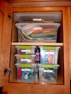 an organized cabinet with plastic bins and file folders in the bottom shelf area