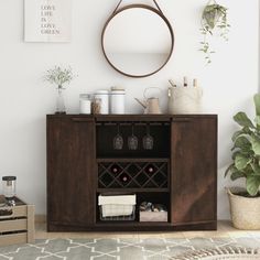 a wooden cabinet with wine glasses and bottles on it next to a potted plant