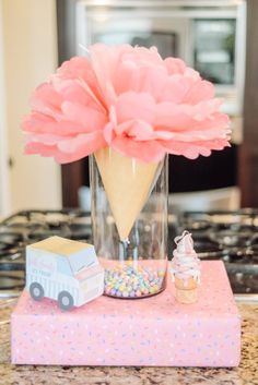 an ice cream cone with a large pink flower in it on a table next to other items