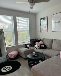 a living room with grey couches and pink pillows on the floor next to large windows