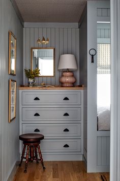 a bedroom with gray painted walls and wooden flooring, along with a small stool in front of the dresser