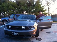 a man standing next to a silver mustang