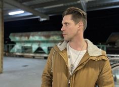 a man standing in an empty parking lot wearing a brown jacket and white t - shirt