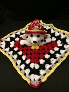 a crocheted teddy bear wearing a fireman's hat on top of a blanket