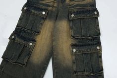 Wide-leg jeans in a unique olive-tinted wash with prominent cargo-style pockets. Features four large patch pockets with button closures on the thighs, combining denim and utility wear aesthetics. The jeans have a high waist and a relaxed, wide-leg silhouette. A central faded panel adds depth to the wash, while distressed details on the thighs and knees create a worn-in look. The bottom hems feature abstract, leaf-like faded patterns. Blends rugged workwear elements with trendy oversized denim fo Vintage Cargo Jeans For Streetwear, Vintage Baggy Cargo Jeans With Pockets, Vintage Straight Leg Cargo Jeans With Side Pockets, Vintage Cargo Jeans With Patch Pockets For Streetwear, Brown Utility Jeans With Side Pockets, Vintage Cotton Cargo Jeans With Multiple Pockets, Brown Utility Cargo Style Jeans, Vintage Dark Wash Jeans With Cargo Pockets, Vintage Denim Cargo Jeans With Pockets