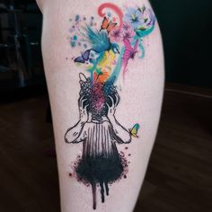 a woman's thigh with an artistic tattoo design on her leg and colorful paint splatters