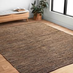 a large brown rug in the corner of a room next to a window with a potted plant