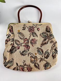 This bohemian, 1970s tapestry handbag is a true statement piece. The brown lucite top handle adds a touch of elegance, while the large fabric body is adorned with beautiful flowered branches and leaves on a light brown background. The tapestry design is sure to catch the eye and add a touch of vintage charm to any outfit. With a spacious 11 inches by 12 inches size, it's perfect for carrying all your daily essentials. Expected wear for a vintage item with minor surface wear on the frame. See pic Elegant Luxury Tapestry Bag, Vintage Tapestry Bag For Everyday, Vintage Beige Tapestry Bag, Vintage Beige Handheld Shoulder Bag, Beige Vintage Bag With Top Carry Handle, Vintage Beige Handheld Bag, Vintage Beige Satchel With Handles, Vintage Beige Satchel With Top Carry Handle, Vintage Beige Satchel