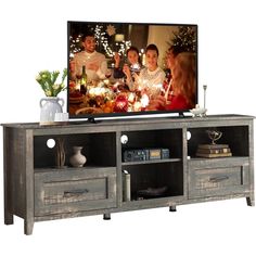 an entertainment center with a large television on it's stand and two people sitting in the background