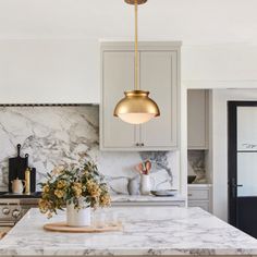 a kitchen with marble counter tops and gold pendant lights hanging from the ceiling over the island