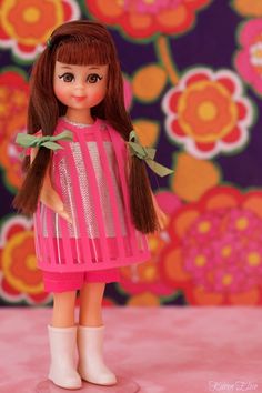 a doll with long brown hair wearing a pink dress and green bow standing in front of a flowered background