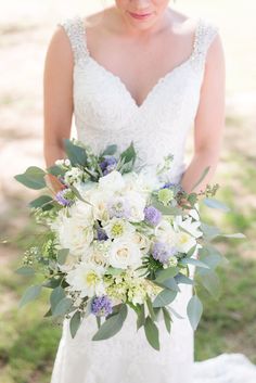 a bride holding a bouquet of white and purple flowers