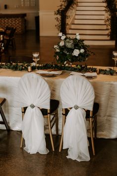 the chairs are covered with white chiffon sashes and place settings at the head table