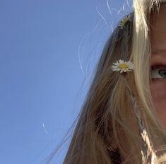 a girl with long blonde hair and a flower in her hair looks up into the sky