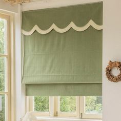 a window with green roman shades in a white room next to a large window sill