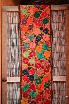 an orange and red quilt hanging on a bamboo wall next to a wooden door with shutters