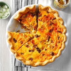 a quiche on a white plate with a slice missing from it next to a bowl of onions