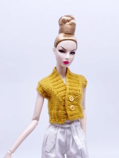 a doll with blonde hair wearing white pants and a yellow sweater on top of her head