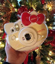 someone holding up a camera in front of a christmas tree with red bows on it