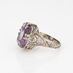 Stylish and finely detailed Art Deco amethyst ring crafted in 18 karat white gold (circa 1920s to 1930s).  Amethyst measures 12.5mm x 8.5mm. Note: light surface abrasions to the amethyst (visible under a 10x loupe).  The square cut amethyst is perched upon a filigree gallery. Charming & intricate pierced floral motifs make this a great for wear during the day or for a glam evening look. The medium rise ring (7mm - 0.27 inches) sits comfortably on the finger.   The ring is in good condition and was recently light cleaned and polished.   Particulars:  Weight: 3.7 grams  Stones:  Amethyst measures 12.5mm x 8.5mm. Note: light surface abrasions to the amethyst (visible under a 10x loupe).  Size & Measurements: The ring is a size 5 1/2 (sizable). The mount measures 12.5mm in length (0.49 inches) Vintage Wedding Rings 1920s White Gold, Art Deco Amethyst Ring, Art Nouveau Rings, 1920s Wedding Ring, Goth Wedding Rings, Goth Wedding Ring, Amethyst Wedding Rings, Filigree Wedding Ring, Hippie Goth